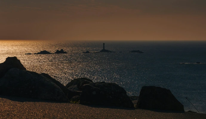 the sun is setting over the ocean and rocks